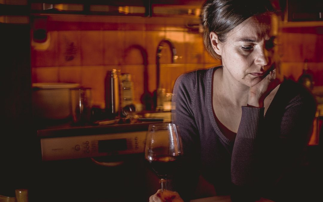 Sad woman looking at a glass of wine, struggling with the mental battle with alcohol